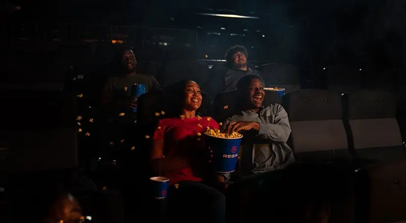 Excited moviegoers experiencing the immersive 4DX effects at a Regal cinema, with dynamic seating and sensory elements like moving chairs and flying popcorn.